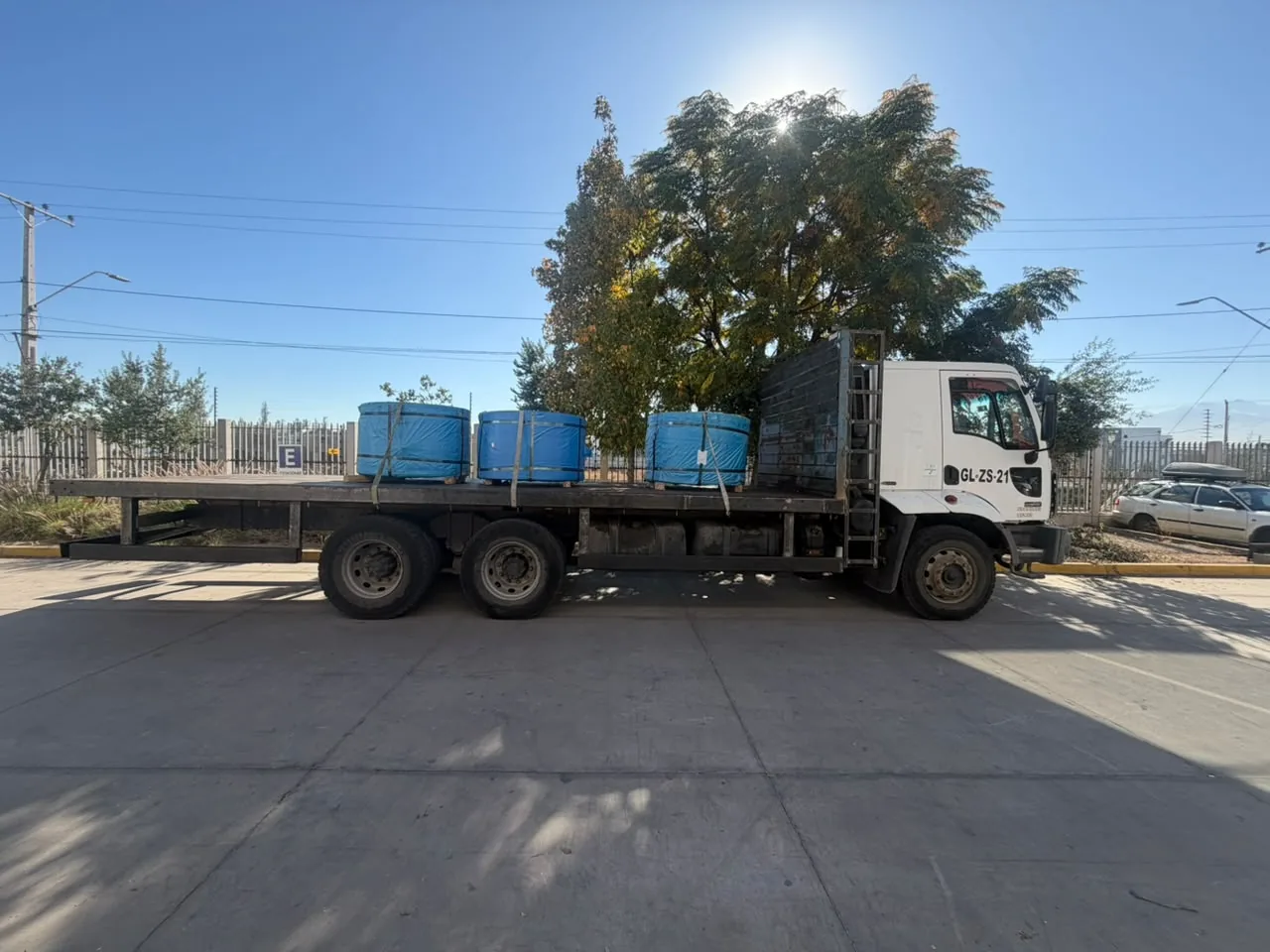 Camión plano con tres bobinas envueltas en plástico azul y amarradas con correas