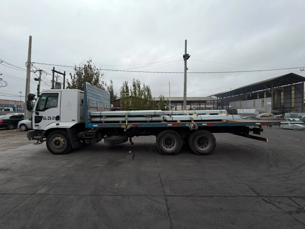 Camión plano con perfiles metálicos amarrados con correas en un patio industrial