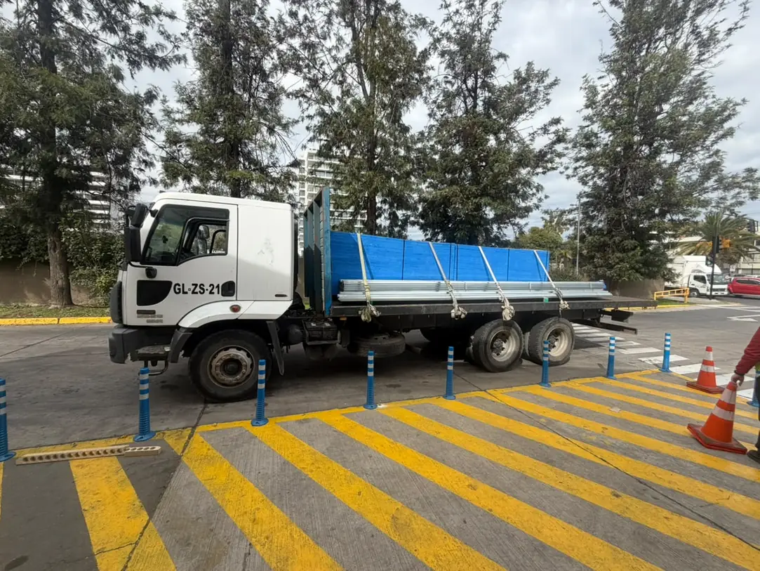 Camión plano con paneles azules y perfiles metálicos amarrados con correas, estacionado en una calle