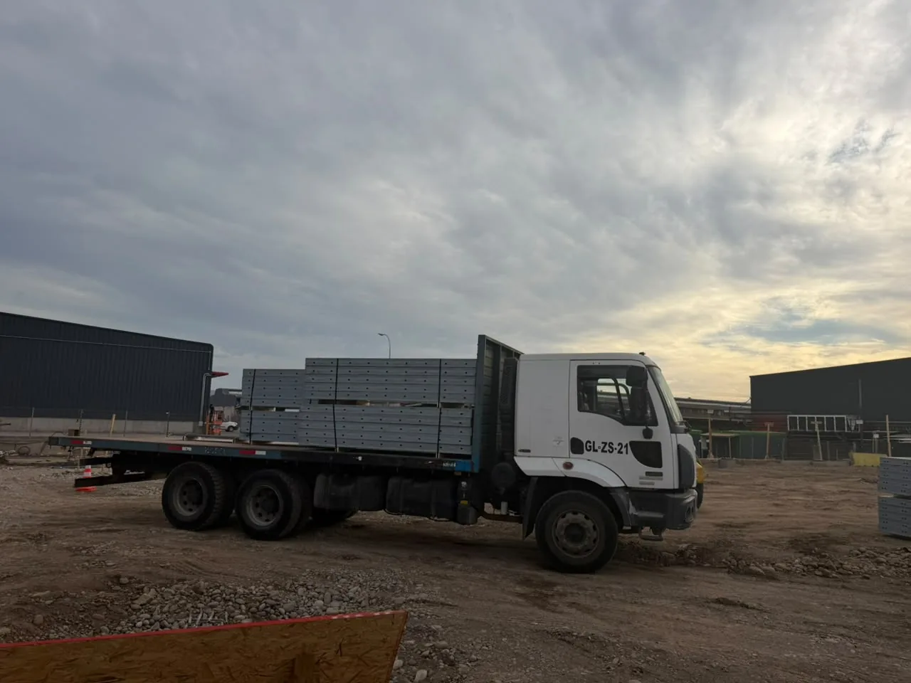 Camión plano con paneles metálicos grises apilados en una obra