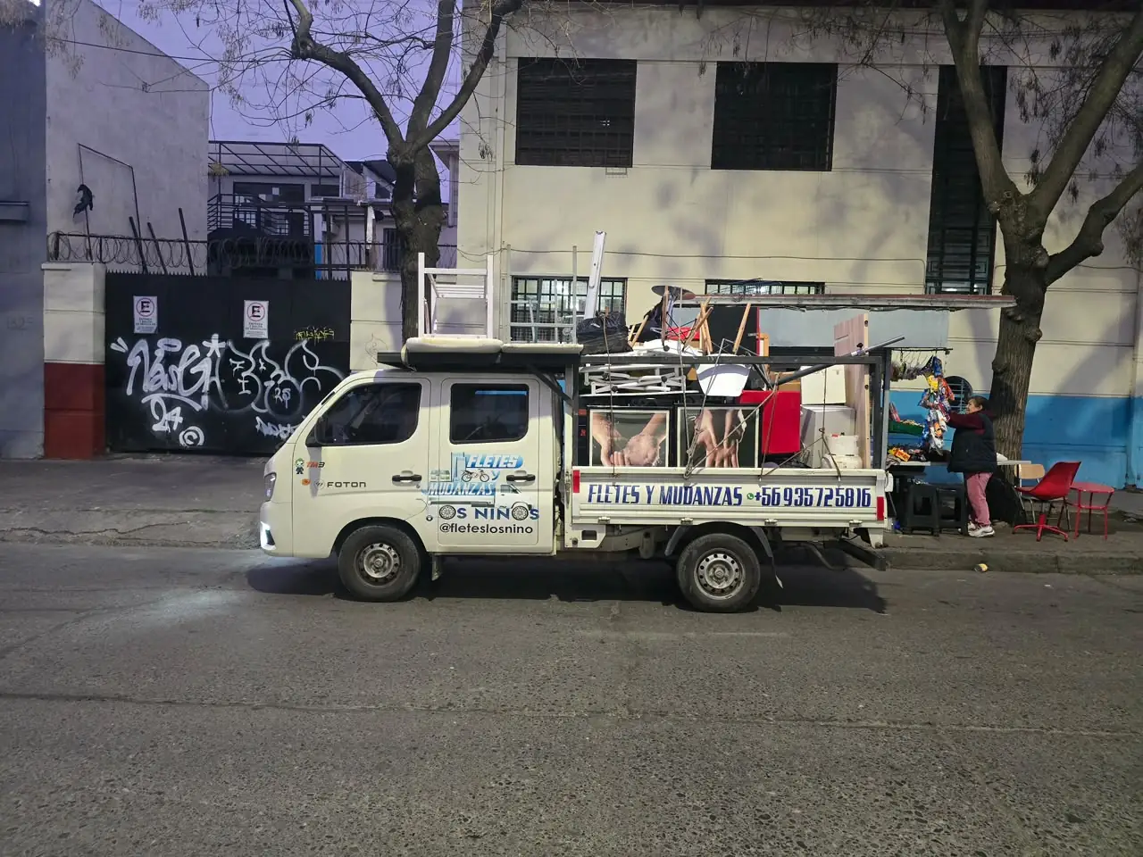 Camioneta Foton de doble cabina con la plataforma cargada de sillas, un mueble y electrodomésticos, estacionada en una calle