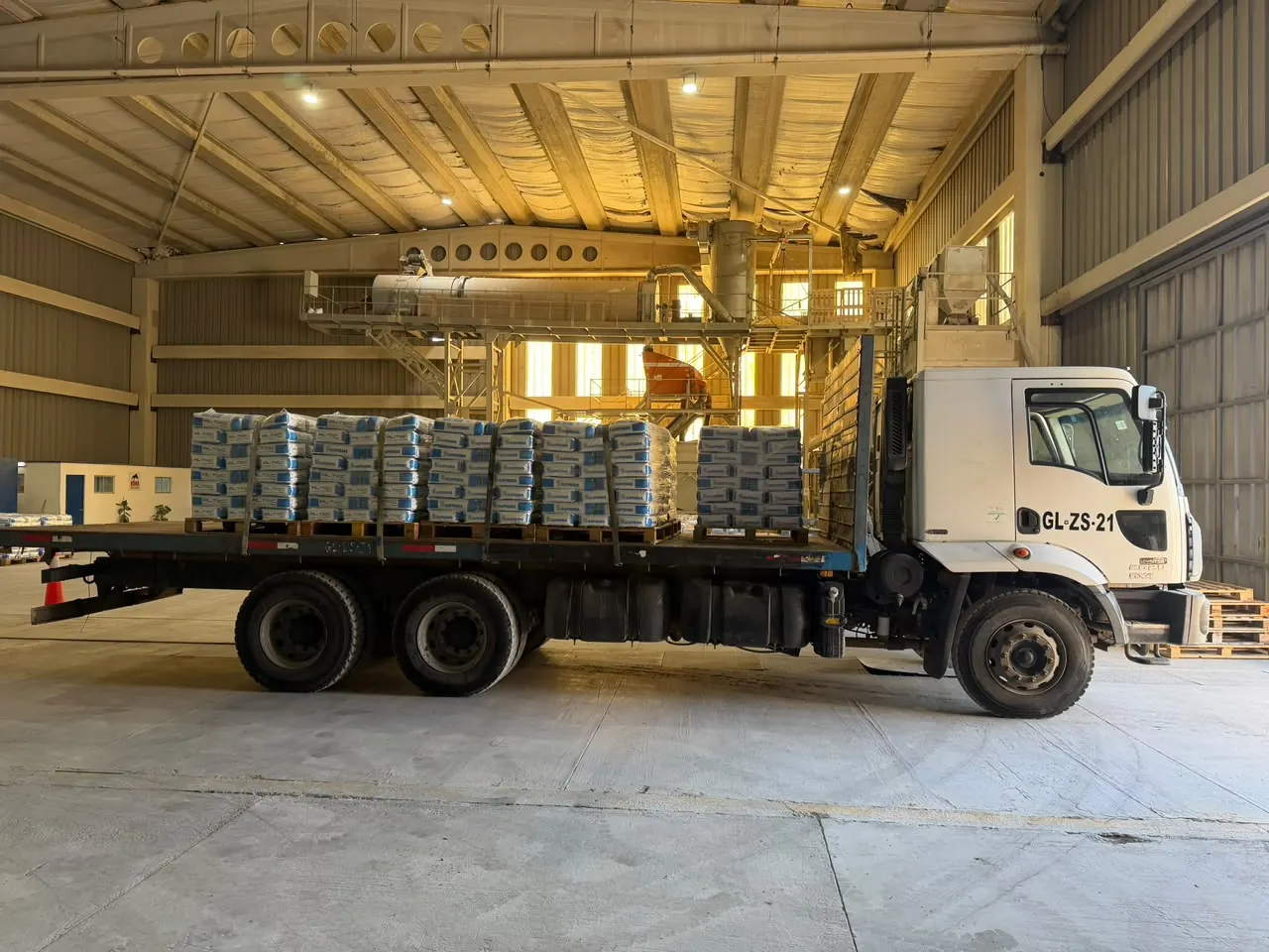 Camión plano con pallets de sacos apilados y amarrados con correas dentro de una planta industrial